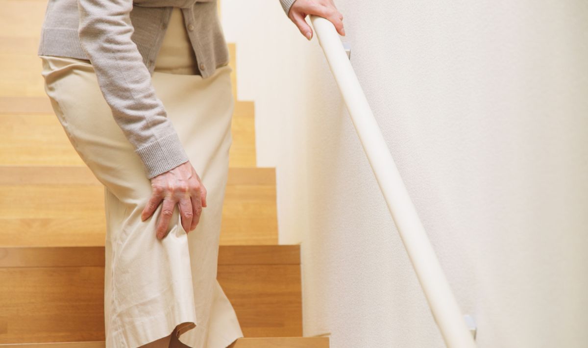 Female holding onto stair handrail and holding onto knee highlighting knee pain