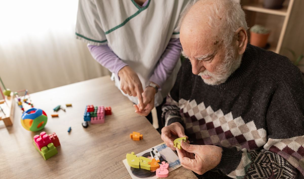Elderley male working on a puzzle with help of an instructor